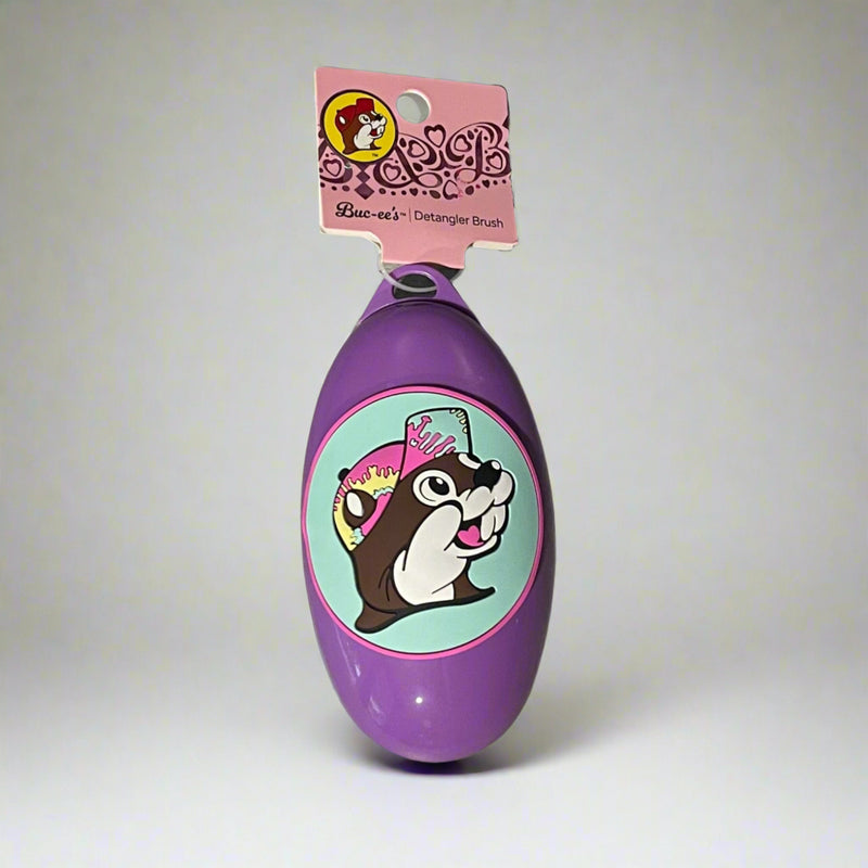 Buc-ee’s detangler brushes in two colors: one black with Buc-ee in a red cap, and one purple with Buc-ee surrounded by pink hearts, shown from front and back views.

