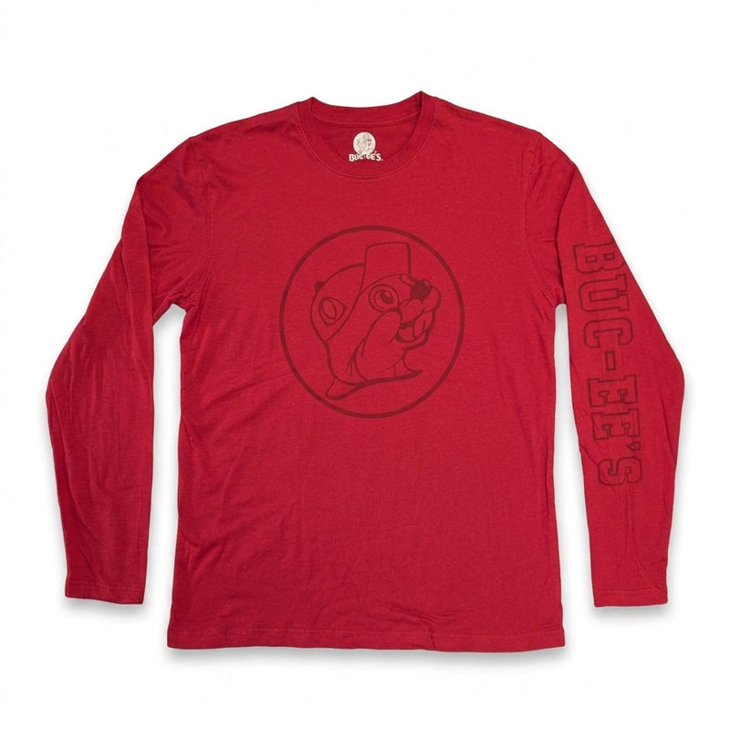 A top-down view of a plain red Buc-ee's long-sleeve crewneck shirt lying flat on a white background. The shirt features a dark red circular Buc-ee's beaver logo printed on the chest and dark red "BUC-EE'S" text along the left sleeve.