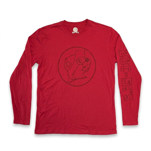 A top-down view of a plain red Buc-ee's long-sleeve crewneck shirt lying flat on a white background. The shirt features a dark red circular Buc-ee's beaver logo printed on the chest and dark red "BUC-EE'S" text along the left sleeve.