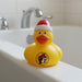 Yellow Buc-ee’s rubber duck wearing a red and white Santa hat, featuring the Buc-ee’s beaver logo on the front, sitting on the edge of a bathtub.
