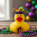 Yellow Buc-ee’s rubber duck wearing a colorful Mardi Gras jester hat with bells and the Buc-ee’s logo on the front, displayed on a table surrounded by purple, green, and gold bead necklaces.