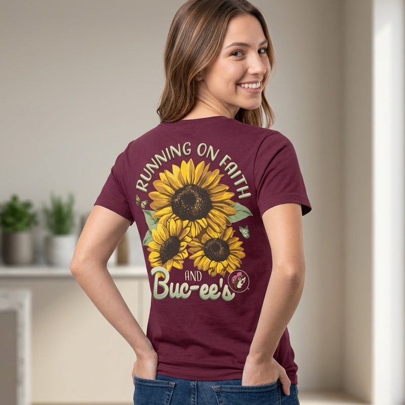 Back view of a maroon Buc-ee's T-shirt featuring bright yellow sunflowers, butterflies, the Buc-ee's logo, and text reading "Running on Faith and Buc-ee's."