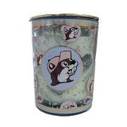 A close-up shot of a Buc-ee’s Blossoms & Bows scented candle in a teal glass jar with a gold lid. The jar is decorated with a pattern of green vines, purple flowers, and pink bows. A central circular emblem features the Buc-ee the Beaver mascot wearing a pink hat against a light blue background, bordered by a gold rim. The wax inside is a pale, off-white color. Displayed on a clean white background.