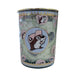 A close-up shot of a Buc-ee’s Blossoms & Bows scented candle in a teal glass jar with a gold lid. The jar is decorated with a pattern of green vines, purple flowers, and pink bows. A central circular emblem features the Buc-ee the Beaver mascot wearing a pink hat against a light blue background, bordered by a gold rim. The wax inside is a pale, off-white color. Displayed on a clean white background.