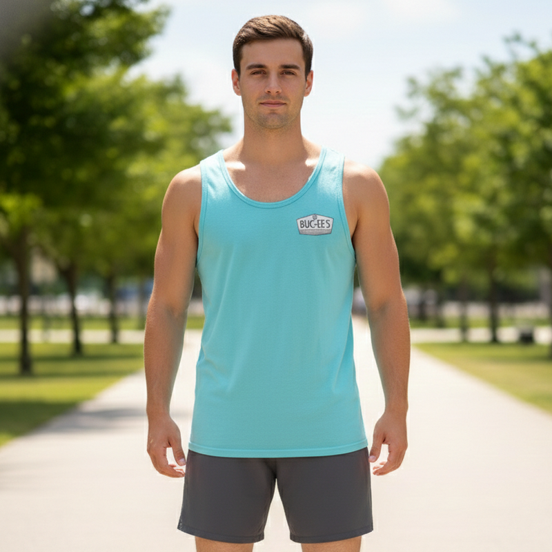 Man wearing a light blue tank top and dark shorts standing on a path with greenery in the background