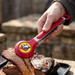 A lifestyle photo of a person using Buc-ee's red and stainless steel serving tongs with a beaver logo to lift a slice of sliced brisket from a black tray on a wooden table.