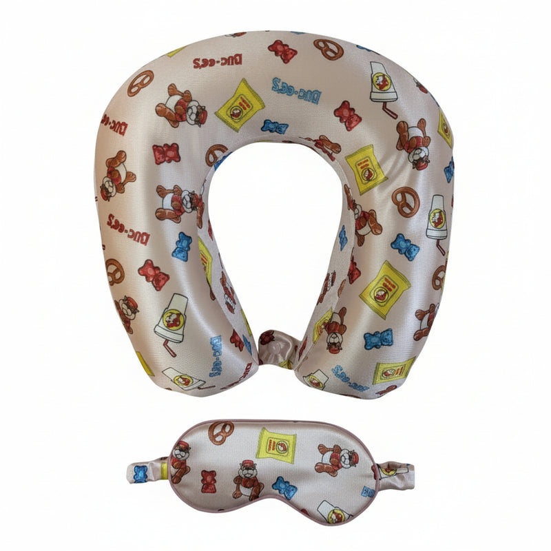 Buc-ee’s travel set featuring a silky eye mask and matching U-shaped neck pillow decorated with Buc-ee the Beaver, Beaver Nuggets bags, gummy bears, pretzels, and snack icons.