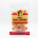 A clear 8 oz resealable bag of Buc-ee's Peach Sour Gummies. The label features the famous Buc-ee's beaver logo and bold red text against a yellow background. Inside, the bag is filled with round, sugar-coated gummies that are half-pink and half-yellow, resembling small peaches. Displayed on a clean white background.