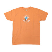 An orange short-sleeve crew neck t-shirt laid flat on a white surface. The front of the shirt features a small, centered chest graphic showing a white highway shield outline containing the Buc-ee's beaver mascot in a blue baseball cap, with the text "Buc-ee's South Carolina" curved beneath it.