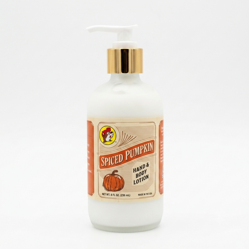 A square, close-up photograph of a bottle of Buc-ee's "Spiced Pumpkin" hand and body lotion centered against a solid white background. The bottle is made of frosted glass containing white lotion, topped with a shiny gold collar and a white pump dispenser. The vintage-style cream paper label features the Buc-ee's beaver logo, the words "SPICED PUMPKIN" in bold red text, an illustration of an orange pumpkin, and text reading "HAND & BODY LOTION," "NET WT. 8 FL OZ. (236 ML)," and "MADE IN THE USA."