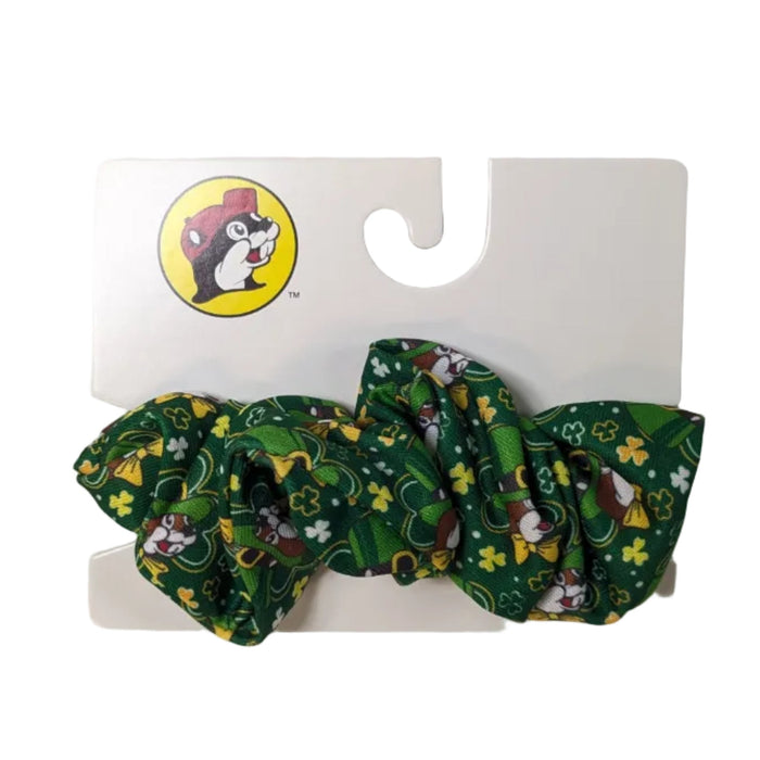 A Buc-ee's green scrunchie with a dense festive print of Buc-ee and shamrocks, attached to a white Buc-ee’s retail display card, displayed on a clean white background.