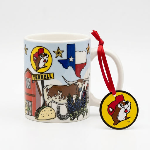 A mini white ceramic mug ornament against a plain white background featuring Texas-themed illustrations, including a Texas flag, a Longhorn steer, bluebonnets, a taco, and a red barn next to a Buc-ee's logo sign reading "TERRELL". A red ribbon tied to the handle holds a round, yellow Buc-ee's beaver head logo tag.