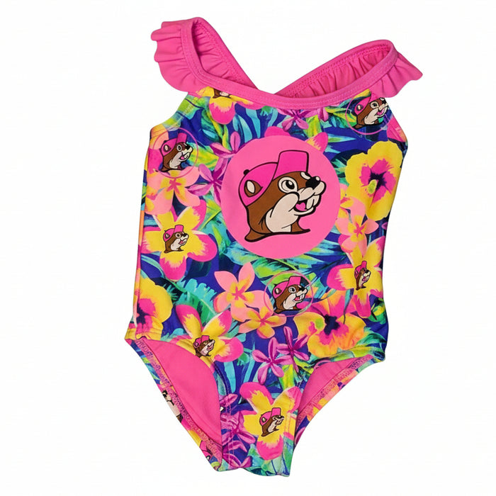 A baby and toddler one-piece swimsuit featuring a vibrant tropical floral pattern with yellow, pink, and purple hibiscus flowers on a blue leafy background. The design includes a large circular pink graphic of the Buc-ee's mascot in a pink hat centered on the chest, bright pink ruffled shoulder straps that cross in the back, and a solid pink interior lining, displayed on a clean white background.