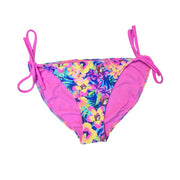 A Buc-ee's Women’s Tropical Floral bikini bottom featuring a vibrant tropical floral print with yellow and pink hibiscus flowers and the Buc-ee's mascot on a blue leafy background. The design includes adjustable bright pink side-tie drawstrings at the hips that tie into bows, allowing for a customizable leg height, and is finished with a solid pink interior lining, displayed on a clean white background.