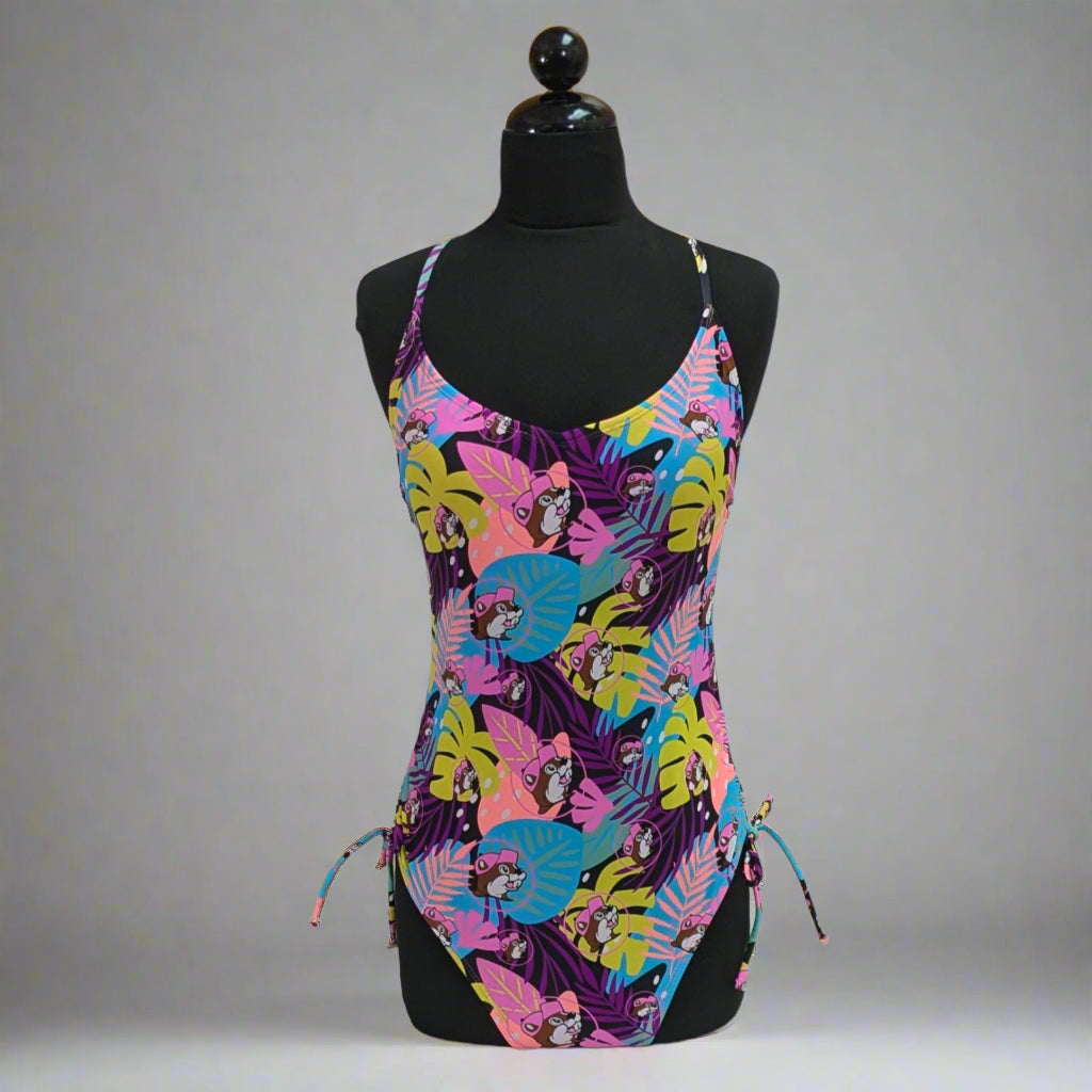 Buc-ee's Tropical One Piece Swim Suit. With Purple, Pink, blue, and yellow palm leaves and Buc-ee's Logo. 