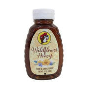 A 12 oz. plastic squeeze bottle of Buc-ee's Wildflower Honey standing upright against a white background. The container is a clear, amber-tinted bottle with distinct ribbed edges on the sides and a white plastic cap. The cream-colored label features a subtle honeycomb pattern, the round Buc-ee's beaver logo, cursive text reading "Wildflower Honey", an illustration of yellow and purple wildflowers, and the text "RAW & UNFILTERED" and "NET WT. 12 OZ. (340g)".