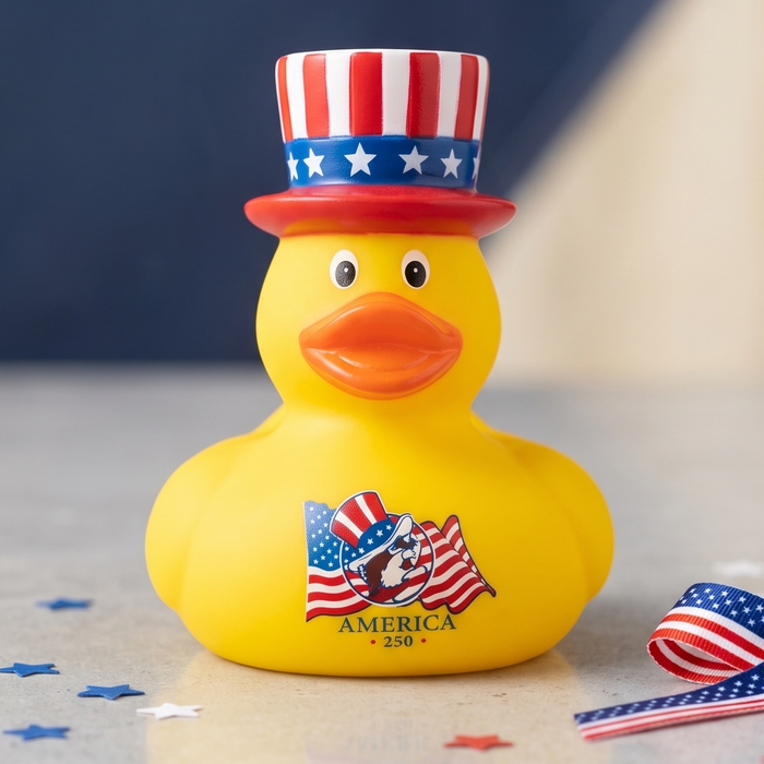Yellow rubber duck with American flag hat and bow on a gray surface