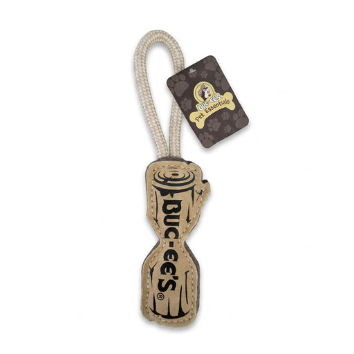 A Buc-ee's Pet Essentials dog toy shaped like a wooden log made of tan leather with "BUC-EE'S" text on the front, attached to an off-white braided rope loop handle.