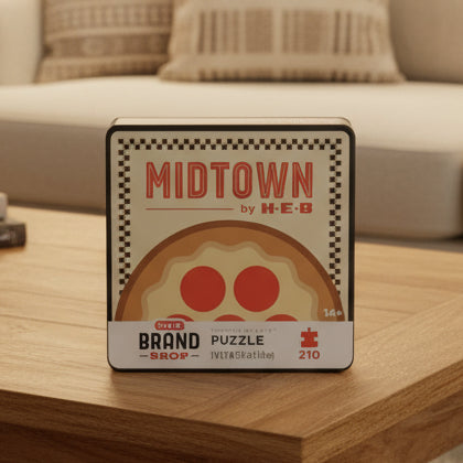 Front view of the H-E-B Midtown by H-E-B Puzzle box featuring a pizza-themed design with pepperoni slices, the words “MIDTOWN by H-E-B,” and “H-E-B Brand Shop Puzzle” on a beige checkered background.