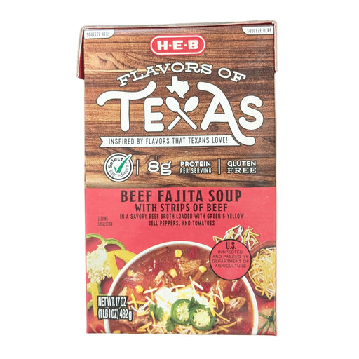 A front-facing view of a 17-ounce carton of H-E-B "Flavors of Texas" Beef Fajita Soup. The packaging features a rustic wood-grain background on the top half with the product title in bold white and red lettering. A prominent "Gluten Free" label and an "8g Protein per serving" callout are visible. The bottom half displays a vibrant serving suggestion of the soup in a bowl, loaded with strips of beef, green and yellow bell peppers, tomatoes, and topped with shredded cheese and jalapeños.
