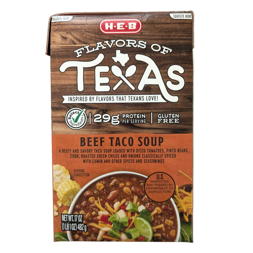 A front-facing, professional studio shot of a 17-ounce carton of H-E-B "Flavors of Texas" Beef Taco Soup on a plain white background. The upper half of the carton features a rustic brown wood-grain texture with the "Flavors of Texas" logo. Key product callouts include "Select Ingredients," "29g Protein per serving," and "Gluten Free." The bottom half has an orange label with the product name and a description of the ingredients, including diced tomatoes, pinto beans, corn, and roasted green chiles.