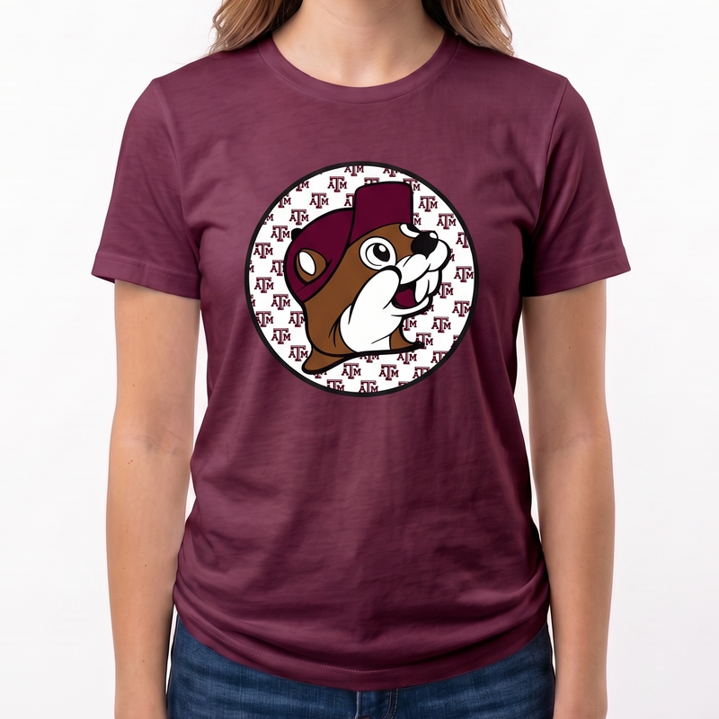 A woman wearing a maroon short-sleeve t-shirt with a circular graphic of a Buc-ee beaver wearing a football helmet, paired with blue jeans, against a plain white background.