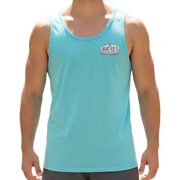 Man wearing a light blue tank top and dark shorts standing on a path with greenery in the background
