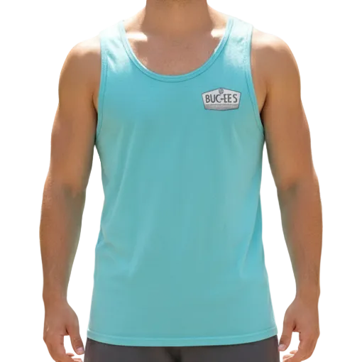 Man wearing a light blue tank top and dark shorts standing on a path with greenery in the background