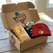 Open cardboard box with 'Texas Snax' branding, containing snacks and a red beanie on a wooden surface.