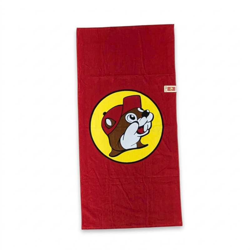 Buc-ee’s classic red beach towel laid flat, with a large yellow circle beaver logo printed in the center