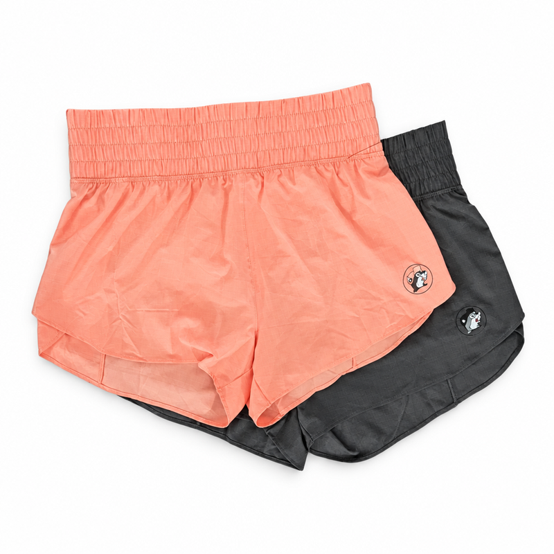 Buc-ee’s Performance Shorts in peach and black with smocked high-rise waistband, curved hem, and beaver logo on the leg
