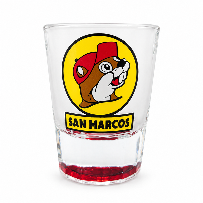 Buc-ee's San Marcos shot glass in clear glass with a red-tinted base and the yellow beaver logo above a San Marcos banner