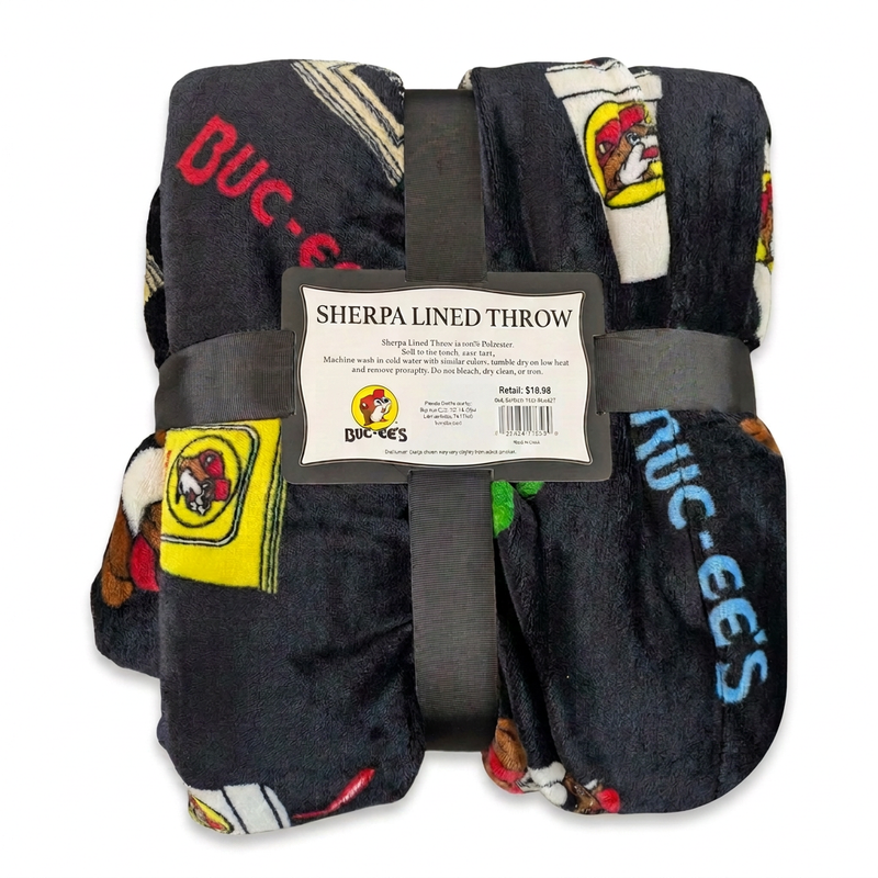 Buc-ee’s Snacks Sherpa Lined Throw blanket in black with Buc-ee’s logos and a snack bag print, folded and tied with a ribbon