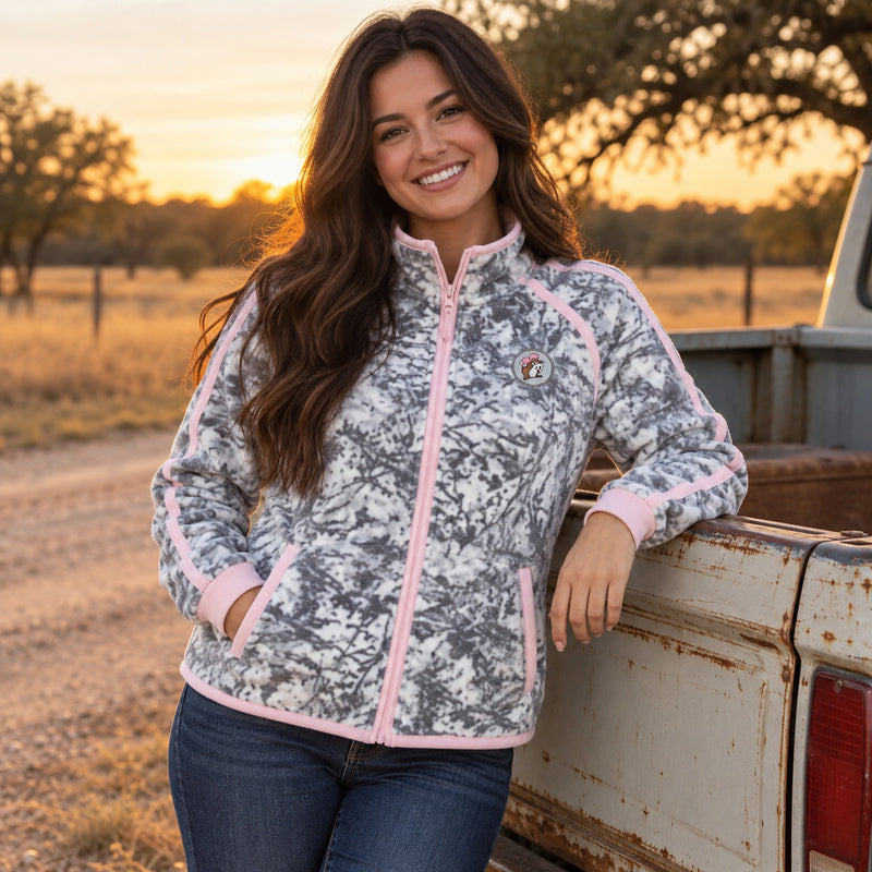 Woman by a ranch truck at sunset wearing the snow camo Buc-ee's fleece jacket