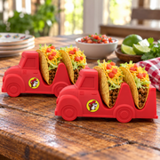 Two red Buc-ee's Taco Truck holders on a rustic wooden kitchen table, each holding two hard-shell tacos with ground beef, lettuce, cheddar and tomato