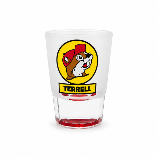 A clear frosted shot glass featuring the yellow circular Buc-ee's beaver logo with a yellow banner underneath reading "TERRELL" in black text, set against a solid white background. The glass features a thick clear base tinted red at the very bottom.