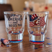 Two shot glasses with patriotic designs on a wooden surface.