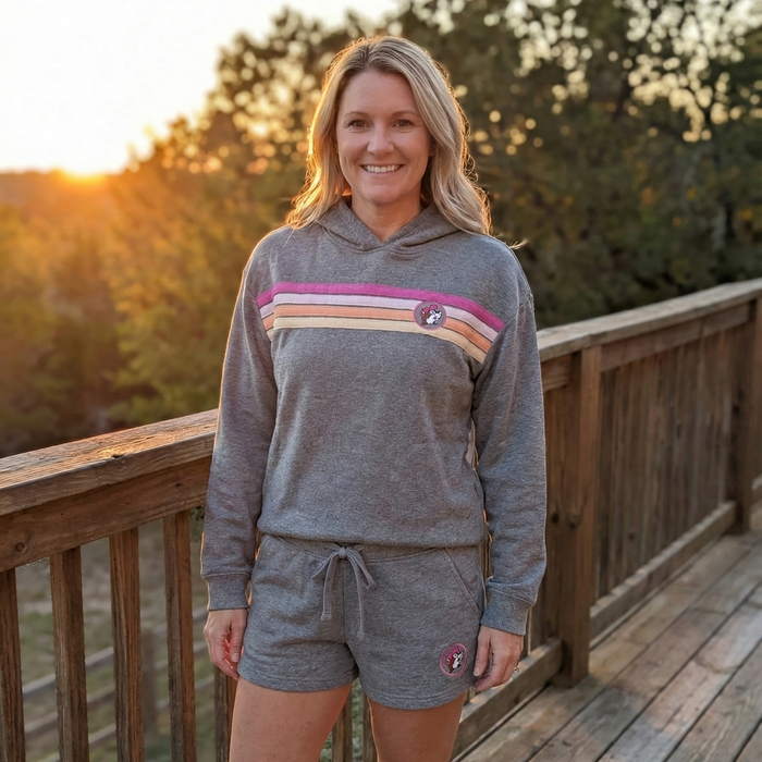 Woman wearing a gray hoodie and shorts set on a wooden deck with a sunset background