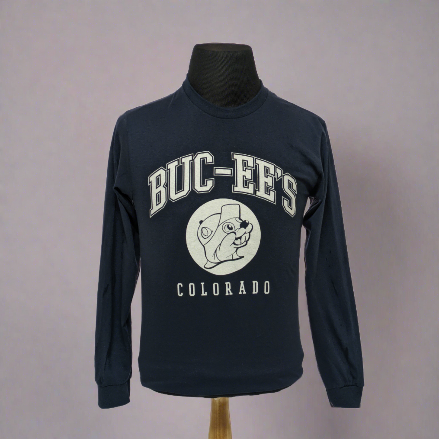 This is a long-sleeved Buc-ee's t-shirt in dark blue. It has bold white text that read "BUC-EE'S" followed by a white Buc-ee's logo, and then in smaller lettering, still in bold the word "COLORADO"